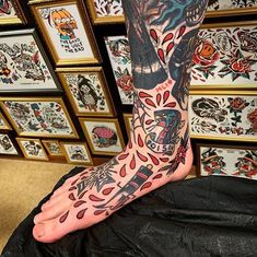 a person with tattoos on their feet and arms is sitting in front of a wall full of framed pictures