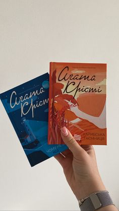 a person holding up two books in their hands, one is orange and the other is blue