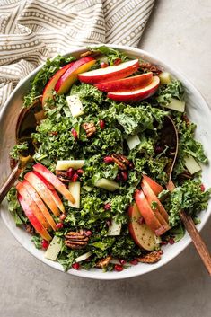 a white bowl filled with salad and sliced apples on top of a gray tablecloth