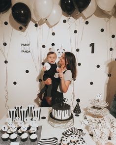 a woman holding a baby in front of a table with black and white decorations on it