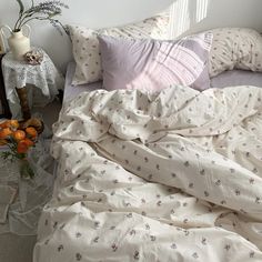 an unmade bed with white sheets and pink flowers on the comforter in front of a window