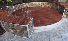 a wooden bench sitting next to a metal fence on top of a stone floor covered in rain