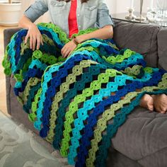 a woman sitting on a couch with a crocheted blanket