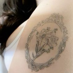 a woman's back with a tattoo on her shoulder and flowers in the frame