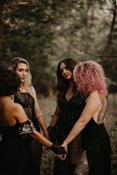 three women in black dresses holding hands with one woman wearing pink hair and the other looking at her