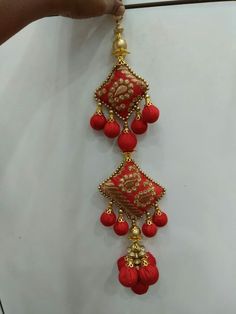 a red and gold necklace is being held by someone's hand in front of a white wall