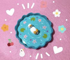 there is a small toy in the middle of a blue bowl on a pink surface