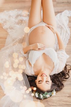 a pregnant woman laying on top of a wooden floor next to a white flower crown