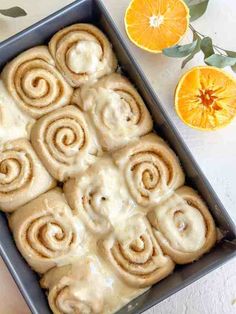 a pan filled with orange cinnamon rolls next to an orange slice and some leaves on the table