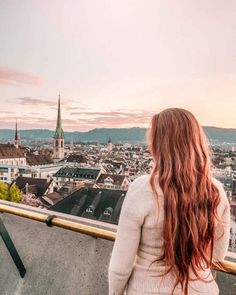 a woman with long red hair standing on top of a building looking at the city