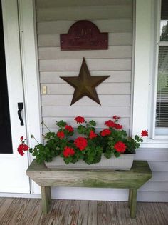 a wooden bench sitting in front of a white house with red flowers growing on it