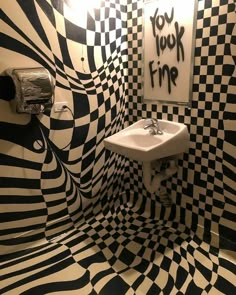 a bathroom decorated in black and white checkered tile with a sink, mirror and towel dispenser