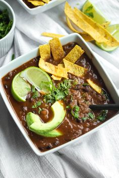 a bowl of chili with tortilla chips and avocado on the side