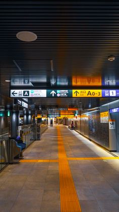 an empty train station at night with signs above the platform and lights on either side