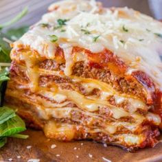 lasagna on a wooden plate with spinach leaves and parmesan cheese