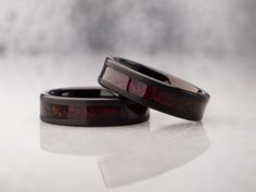 two rings with red and black inlays sitting on top of a white surface