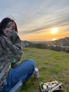 a woman sitting on top of a grass covered field next to a box of sushi