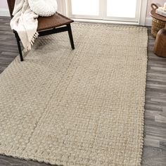 a large rug in the corner of a living room with a chair and window behind it