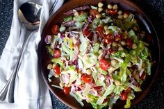 a wooden bowl filled with salad next to a spoon and napkin on top of a table