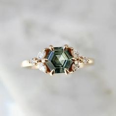 a green and white diamond ring sitting on top of a marble surface