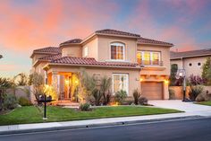 a house with lights on in the front yard and landscaping around it at sunset or dawn