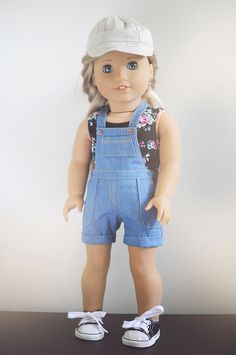 a doll wearing overalls and a hat on top of a wooden table next to a white wall