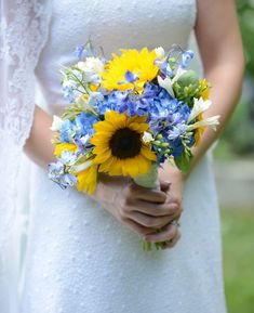 a bride holding a bouquet of sunflowers and blue flowers