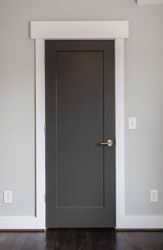 an empty room with a gray door and wooden floors