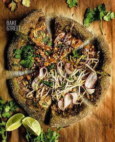 a pizza topped with onions and herbs on top of a wooden cutting board next to limes