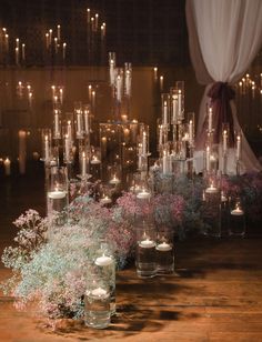 many candles are lit in glass vases on a table