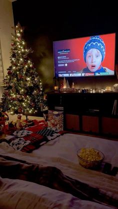 a christmas tree in front of a flat screen tv with a bowl of popcorn on the bed