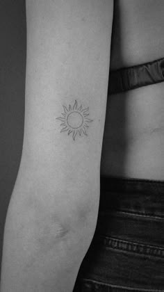 a black and white photo of a woman's arm with a small sun tattoo on it