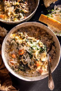 two bowls filled with food on top of a black table next to bread and butter