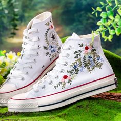 a pair of white sneakers with flowers painted on them sitting in the grass next to some wildflowers