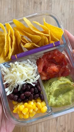 a person holding a plastic container filled with different types of food and chips on top of it