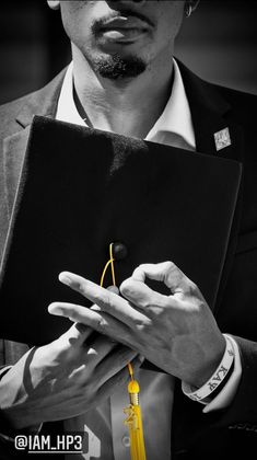 a man in a suit holding a book with a yellow tassel around his neck