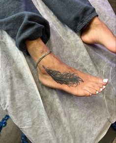 a woman's foot with a feather tattoo on it