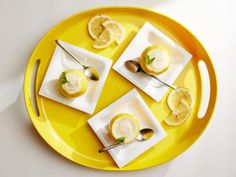 four lemons are sitting on small plates with spoons and silverware in them