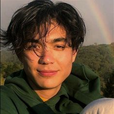 a young man is posing for a photo with a rainbow in the sky behind him