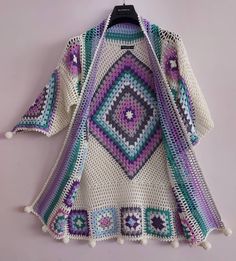 a crocheted sweater hanging on a hanger with a purple and green design