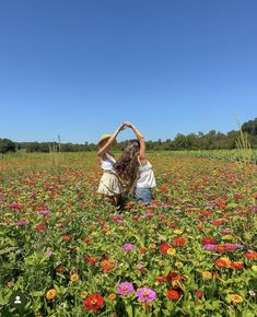 two girls standing in a field full of wildflowers with their hands on their heads