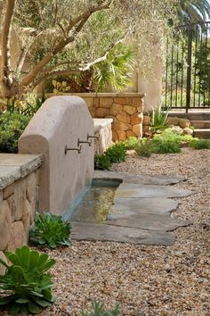 a stone bench sitting in the middle of a garden next to a water feature and trees