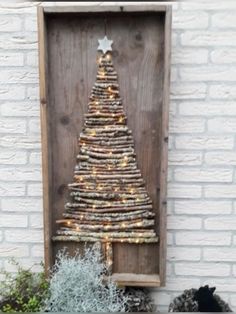 a christmas tree made out of driftwood in front of a white brick wall and potted planter