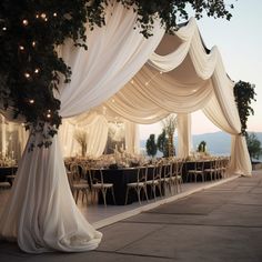 an outdoor dining area with white drapes and lights