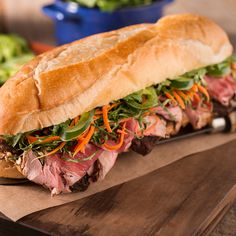 a sandwich with meat, lettuce and carrots on a wooden cutting board