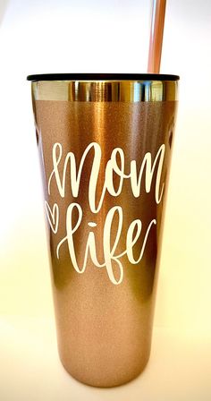 a metallic cup with the words mom and life written on it, next to a straw