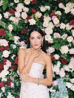 a woman standing in front of a flower covered wall with her hands on her chest