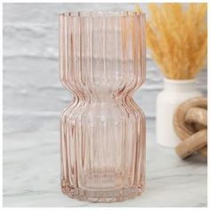 a pink glass vase sitting on top of a white table next to a dried plant