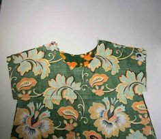 a green floral top with orange and yellow flowers on the front, sitting against a white wall