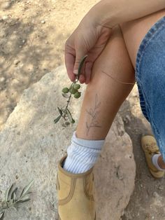 a person sitting on a rock with their legs crossed and holding a plant in her hand